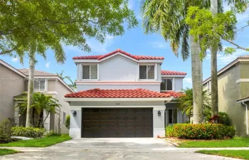 Two-story stucco exterior with a red barrel tile roof, integrated garage, and manicured landscaping