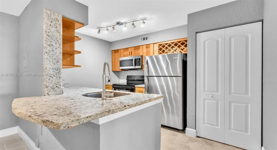 Kitchen featuring a breakfast bar with stone countertop, stainless steel appliances, wood cabinetry, built-in wine rack, and track lighting