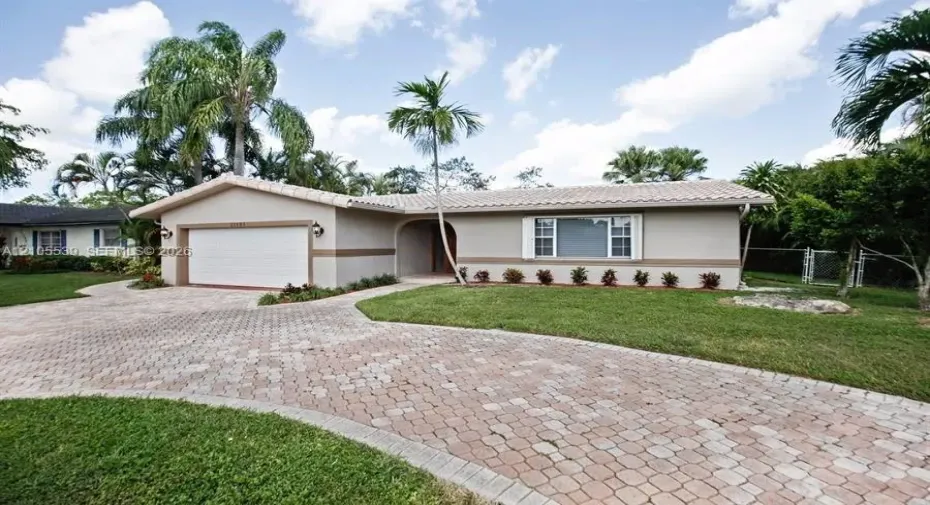 Stucco exterior with a tiled roof, paver driveway, attached garage, and mature landscaping