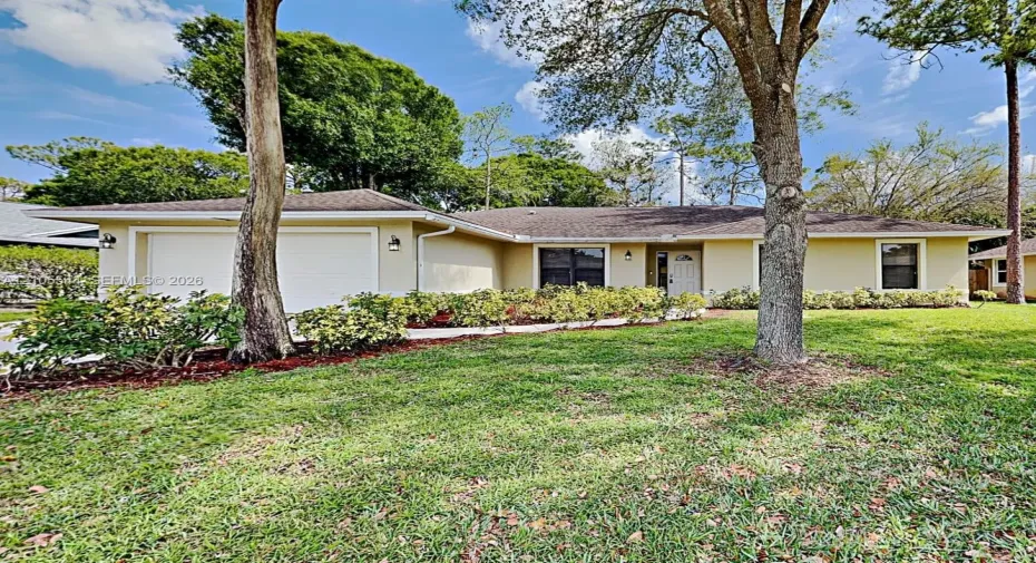 Single-story exterior with a cream stucco finish, two-car garage with white doors, white front entry door, and a shingled roof