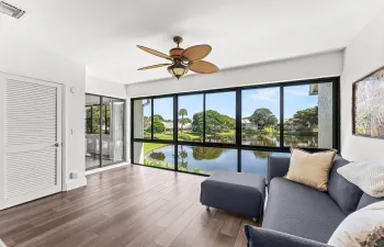 Expansive windows showcasing a water feature and lush landscaping, wood-finish flooring, and a ceiling fan with integrated lighting