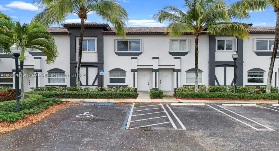 Two-story townhome exterior featuring stucco siding with contrasting trim, arched window accents, tiled roof, and manicured landscaping