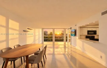 Open-concept interior featuring large-format tile flooring, expansive floor-to-ceiling windows, and a kitchen pass-through with a built-in breakfast bar