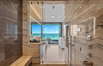 Walk-in shower clad in polished natural stone, featuring a built-in stone bench, integrated recessed shelving, multi-head shower system, and glass enclosure