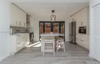 Kitchen featuring white cabinetry, center island with stone countertop, apron-front sink, stainless steel appliances, and wood-finish flooring