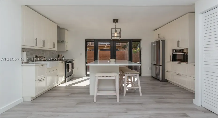 Kitchen featuring white cabinetry, center island with stone countertop, apron-front sink, stainless steel appliances, and wood-finish flooring