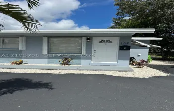 Exterior featuring a painted masonry facade, white entry door with glass insert, horizontal sliding windows, and a concrete stoop with gravel landscaping