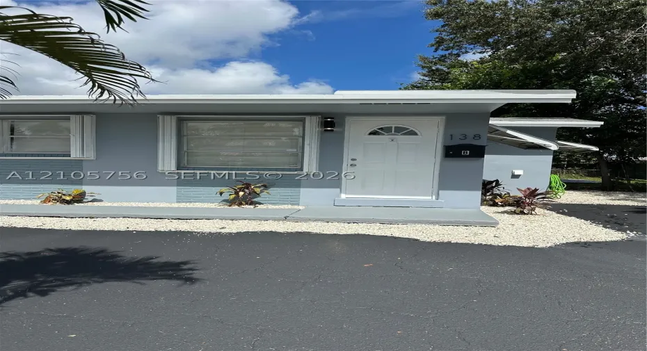 Exterior featuring a painted masonry facade, white entry door with glass insert, horizontal sliding windows, and a concrete stoop with gravel landscaping