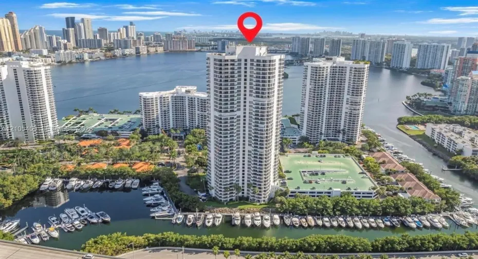 Waterfront high-rise building with multiple balconies, adjacent to a marina with numerous boats