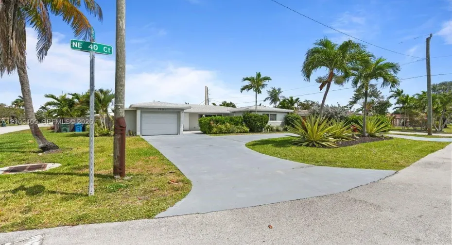 Corner lot with a mature palm tree, manicured landscaping, and a curved driveway leading to a single-car garage