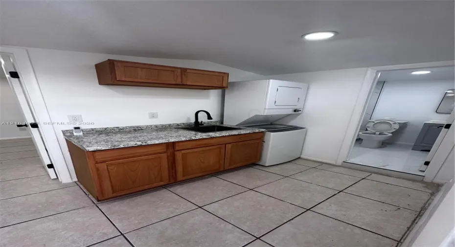 Utility area featuring a granite-finish countertop, wood cabinetry, a black sink with a gooseneck faucet, and a tile floor