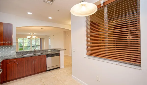 Kitchen featuring granite countertops, wood-finish cabinetry, stainless steel dishwasher, tile flooring, and a window with wood-finish blinds