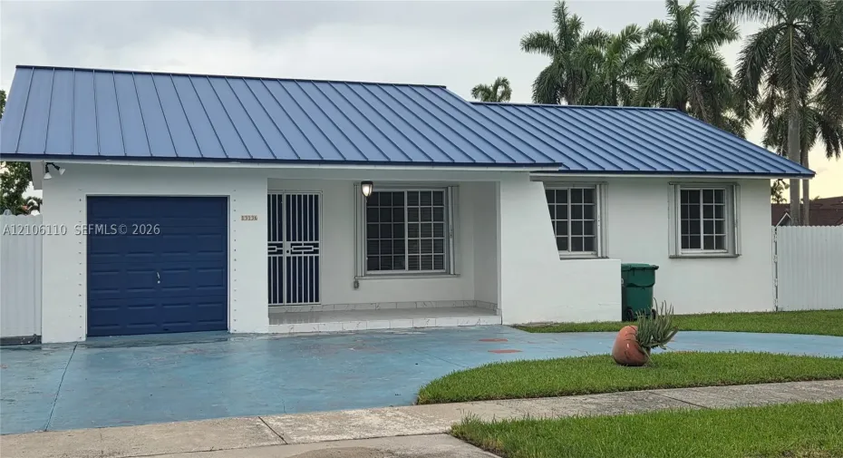 Single-story residence featuring a blue metal roof, stucco exterior, attached garage, covered front porch, and grid-pattern window panes