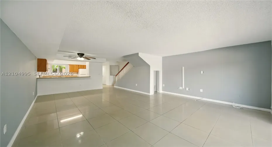 Open interior featuring large-format tile flooring, a kitchen pass-through, neutral wall paint, and a wooden handrail on the staircase
