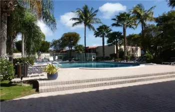 In-ground swimming pool featuring concrete paver decking, multi-level stairs, perimeter fencing, and surrounding palm trees