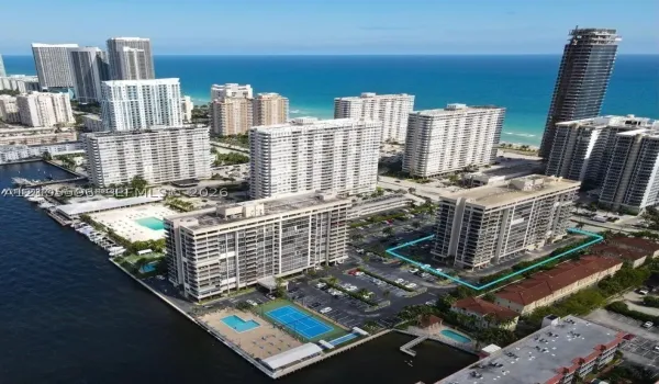 Aerial perspective of a high-rise residential complex located on a waterfront peninsula featuring a swimming pool, tennis court, boat slips, and surface parking