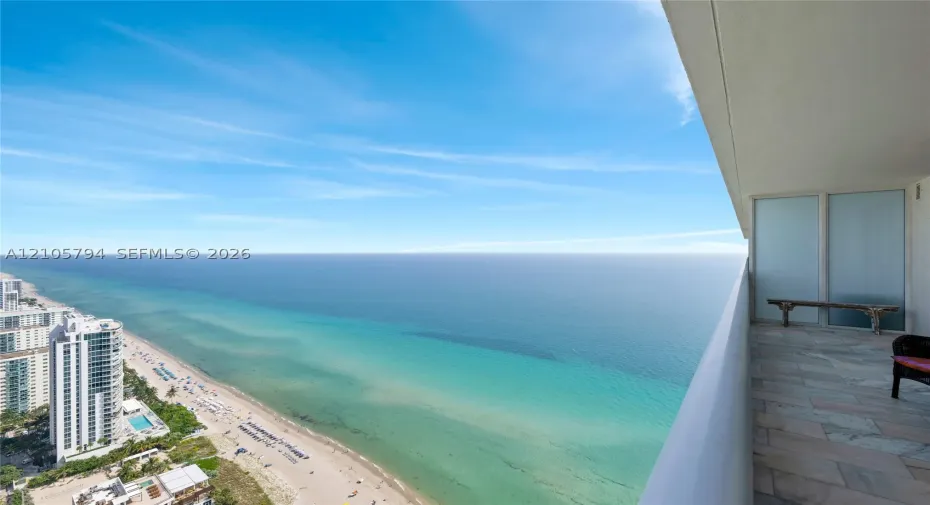 Covered balcony featuring stone tile flooring, frosted glass privacy panel, and expansive ocean scenery