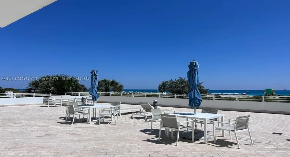 Expansive stone-paved terrace featuring a white metal perimeter railing and coastal horizon