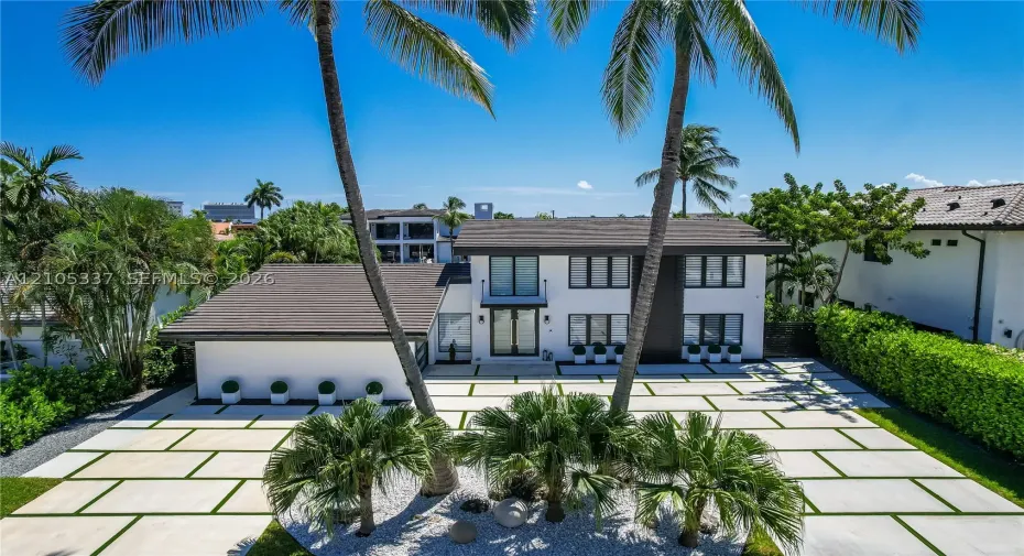 Two-story residence featuring a crisp white exterior, dark-toned roof, paved driveway with grass grid detail, multi-pane windows, and a central balcony
