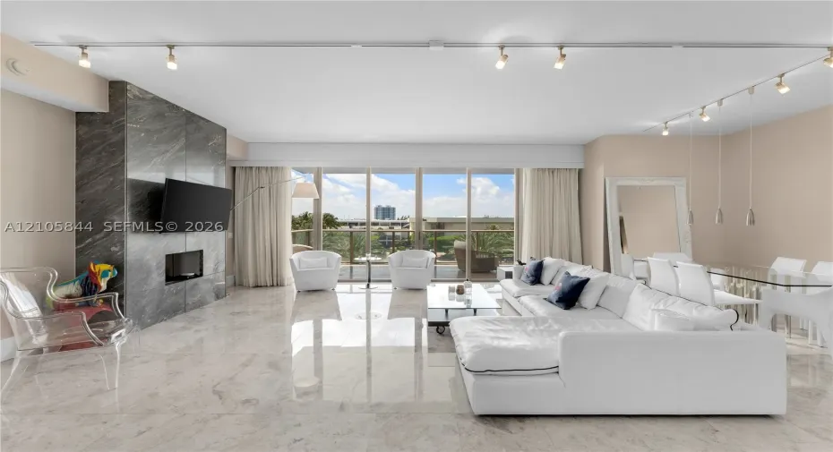 Polished stone flooring, floor-to-ceiling windows, stone-clad fireplace surround, and recessed track lighting