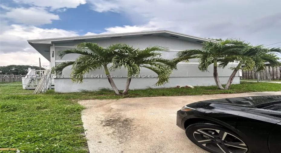 Single-story residence featuring a gabled roofline, concrete driveway, attached staircase with metal railings, and mature palm trees