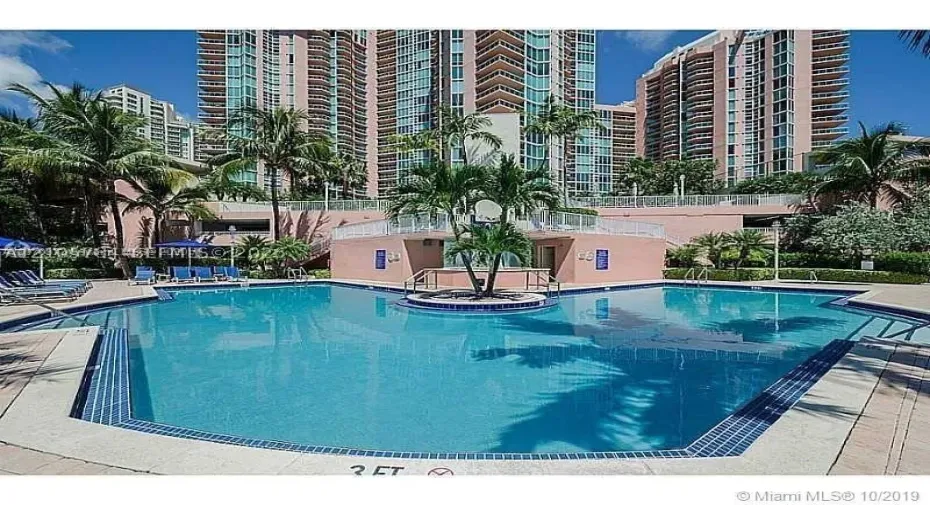 Swimming pool with tile edging, concrete pool deck, and landscaped island with palm trees