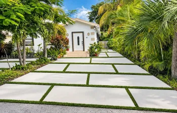 Exterior facade featuring white stucco walls, decorative quoins, a white paneled front door with glass inlay, and a concrete paver driveway with integrated turf strips