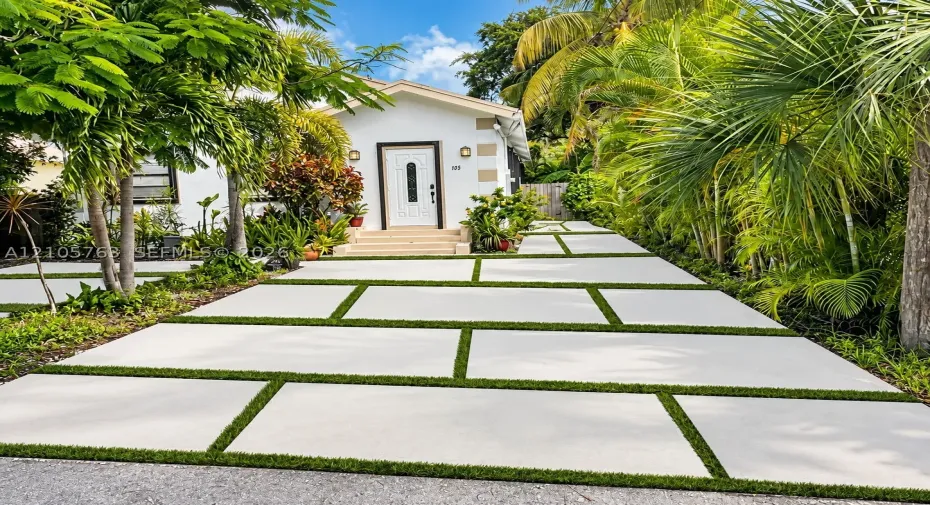 Exterior facade featuring white stucco walls, decorative quoins, a white paneled front door with glass inlay, and a concrete paver driveway with integrated turf strips