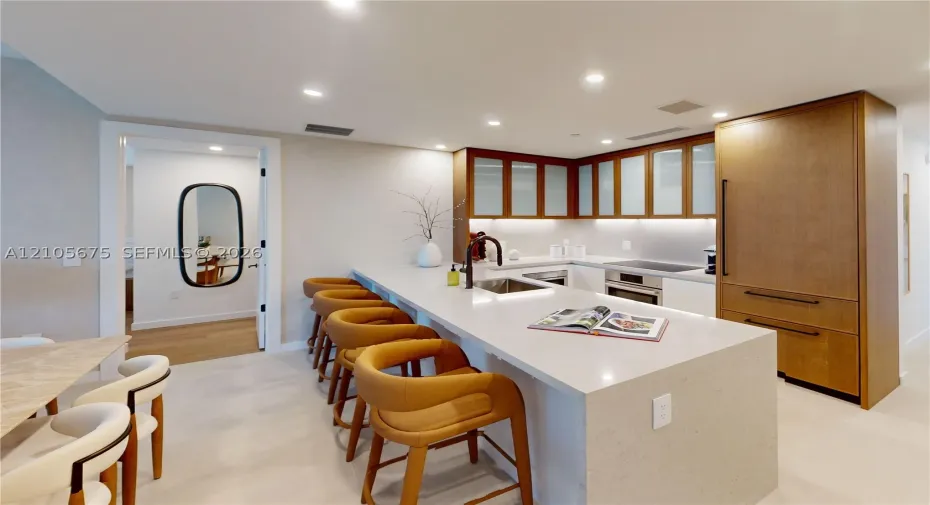 Kitchen featuring an expansive stone-topped island with integrated seating, wood-finish cabinetry, frosted glass cabinet doors, recessed lighting, and a gooseneck faucet. Images are for finish purposes only. Please refer to the floor plan for the layout.