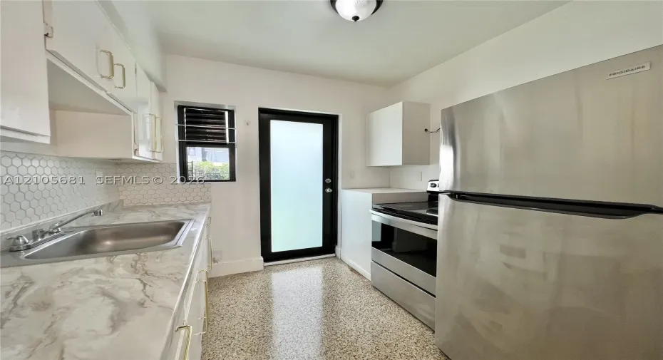 Kitchen featuring white cabinetry, stone-finish countertops, stainless steel appliances, a hexagon tile backsplash, and terrazzo flooring