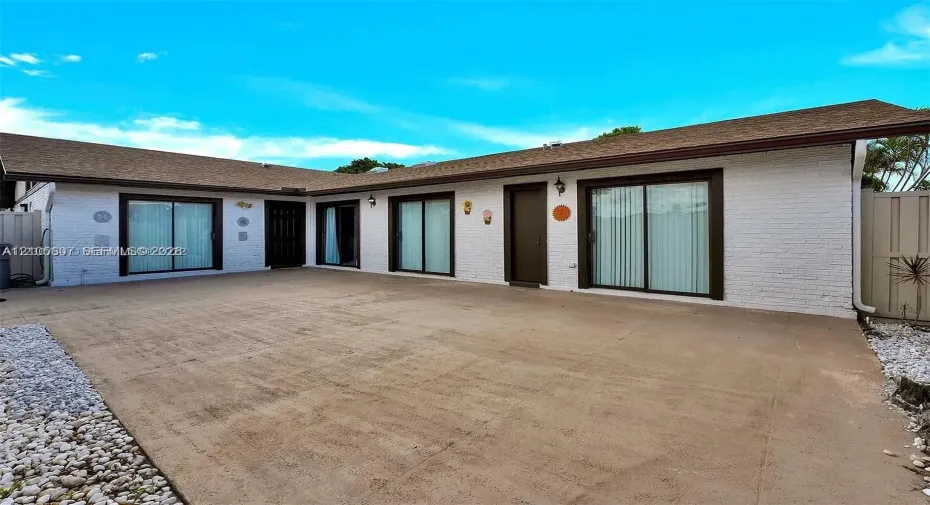 White brick exterior with a brown shingle roof, dark-framed sliding glass doors, and a concrete patio