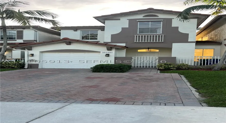 Two-story exterior featuring a stucco finish, arched entryway, a single-car garage, and a herringbone-patterned paver driveway