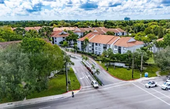 Aerial view of multi-story residential buildings featuring tile roofs, light-toned exterior facades, and extensive landscaping with mature trees and maintained lawns