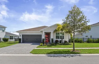 Single-story exterior featuring light-toned vertical siding, a deep-set covered entryway, a multi-car garage with paneled doors, and a decorative paver driveway