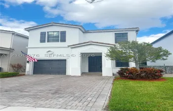 Two-story exterior featuring a light-toned stucco facade, paver driveway, single-car garage, and decorative shutters