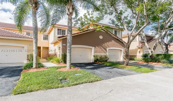 Stucco exterior featuring multi-toned facade, red tile roof, multi-car garage configuration, and manicured landscaping with mature palm trees
