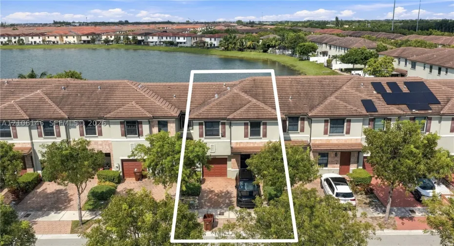 Waterfront townhouse exterior featuring a tiled roof, paver driveway, single-car garage, and stucco facade