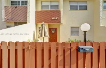 Stucco exterior featuring diagonal wood paneling, multi-pane windows, and a wood-slat privacy fence with an attached mailbox