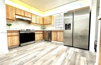 Kitchen featuring wood-finish cabinetry, stone-style backsplash, stainless steel appliances, and wood-finish flooring