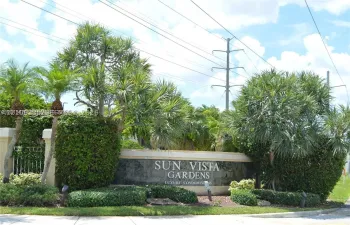 Stone monument sign featuring metallic lettering and integrated landscape lighting, surrounded by mature palm trees and manicured shrubbery