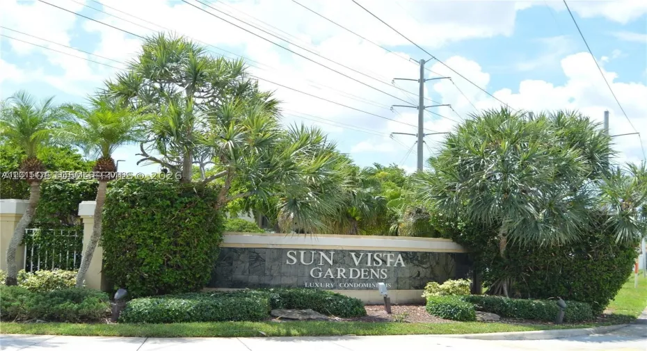 Stone monument sign featuring metallic lettering and integrated landscape lighting, surrounded by mature palm trees and manicured shrubbery