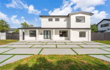 Two-story residence featuring a white exterior, covered front porch, double glass-panel entry doors, and geometric concrete paver driveway with integrated turf strips