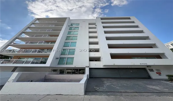 Mid-rise exterior featuring private balconies with metal railings, expansive glass window panels, a secure parking garage, and stone-textured masonry accents
