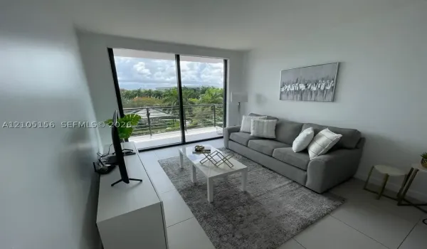 Floor-to-ceiling sliding glass doors, neutral tile flooring, and private balcony with horizontal railing