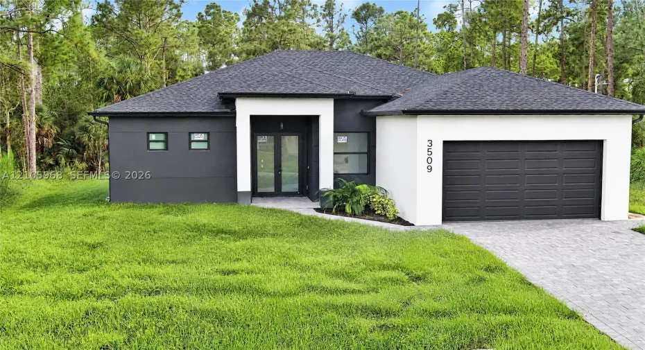Modern single-story exterior featuring high-contrast stucco facade, stone paver driveway, dual-glass entry doors, and a multi-car garage