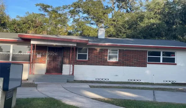 Exterior featuring a mixed-material facade of brick and painted masonry, a covered entry porch with iron support columns, a chimney, and a concrete driveway