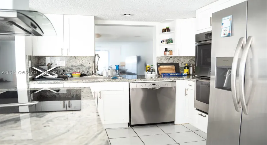 Kitchen featuring white cabinetry, stone countertops, integrated stainless steel appliances, open shelving, and tile flooring