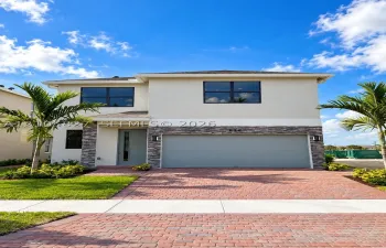 Two-story exterior featuring a light-toned stucco facade, stone veneer accents, a paver driveway, and a two-car garage