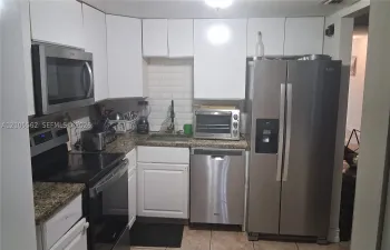 Kitchen featuring white cabinetry, stainless steel appliances, speckled stone-finish countertops, and a white subway tile backsplash