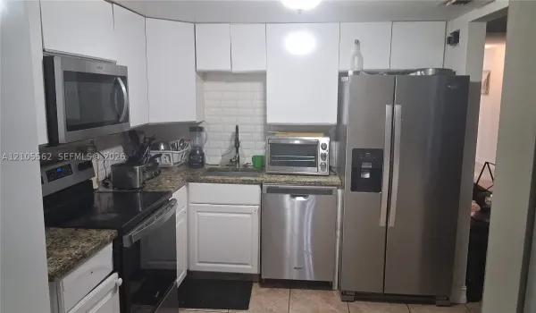 Kitchen featuring white cabinetry, stainless steel appliances, speckled stone-finish countertops, and a white subway tile backsplash